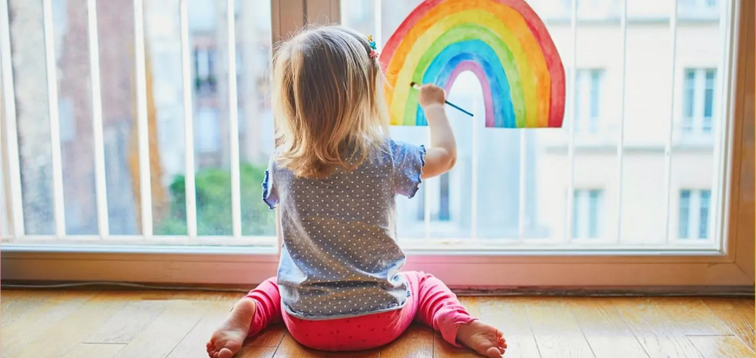 Child painting rainbow on window