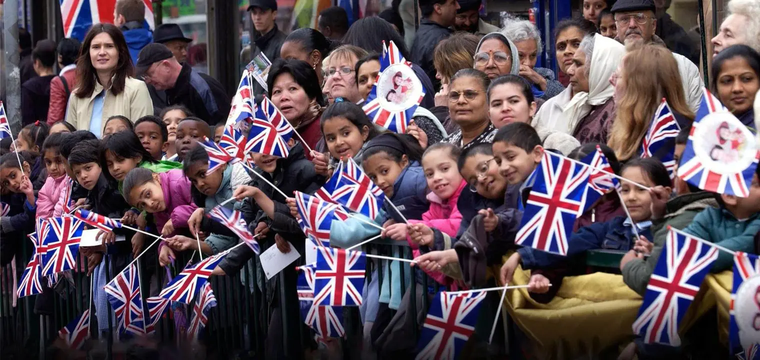 A diverse group of adults and children waving Union Jacks at an open air event