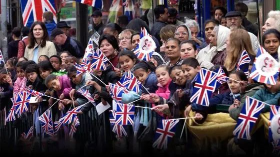 A diverse group of adults and children waving Union Jacks at an open air event