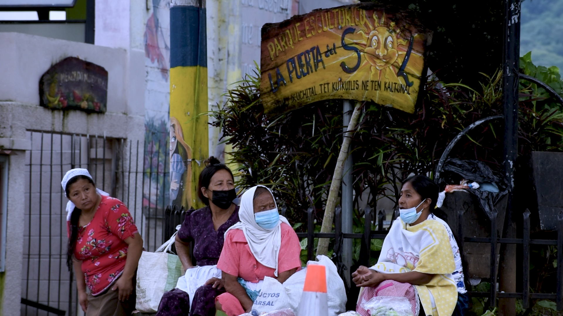 Women sell vegetables under a sign in Spanish and Nahuat