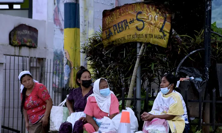 Women sell vegetables under a sign in Spanish and Nahuat