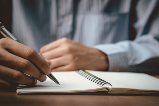 man holds pen over a notepad