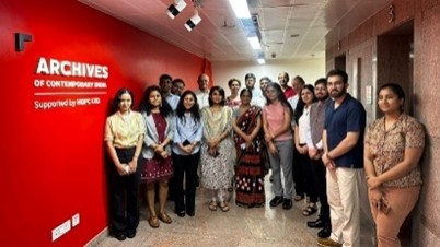 Group of people standing in a hallway next to a red wall with “Archives of Contemporary India” signage