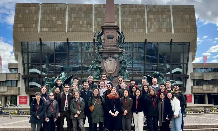 Students and staff standing in front of a large monument and glass building.