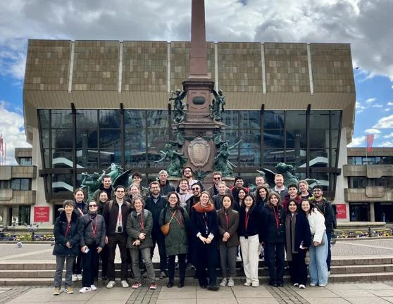 Students and staff standing in front of a large monument and glass building.