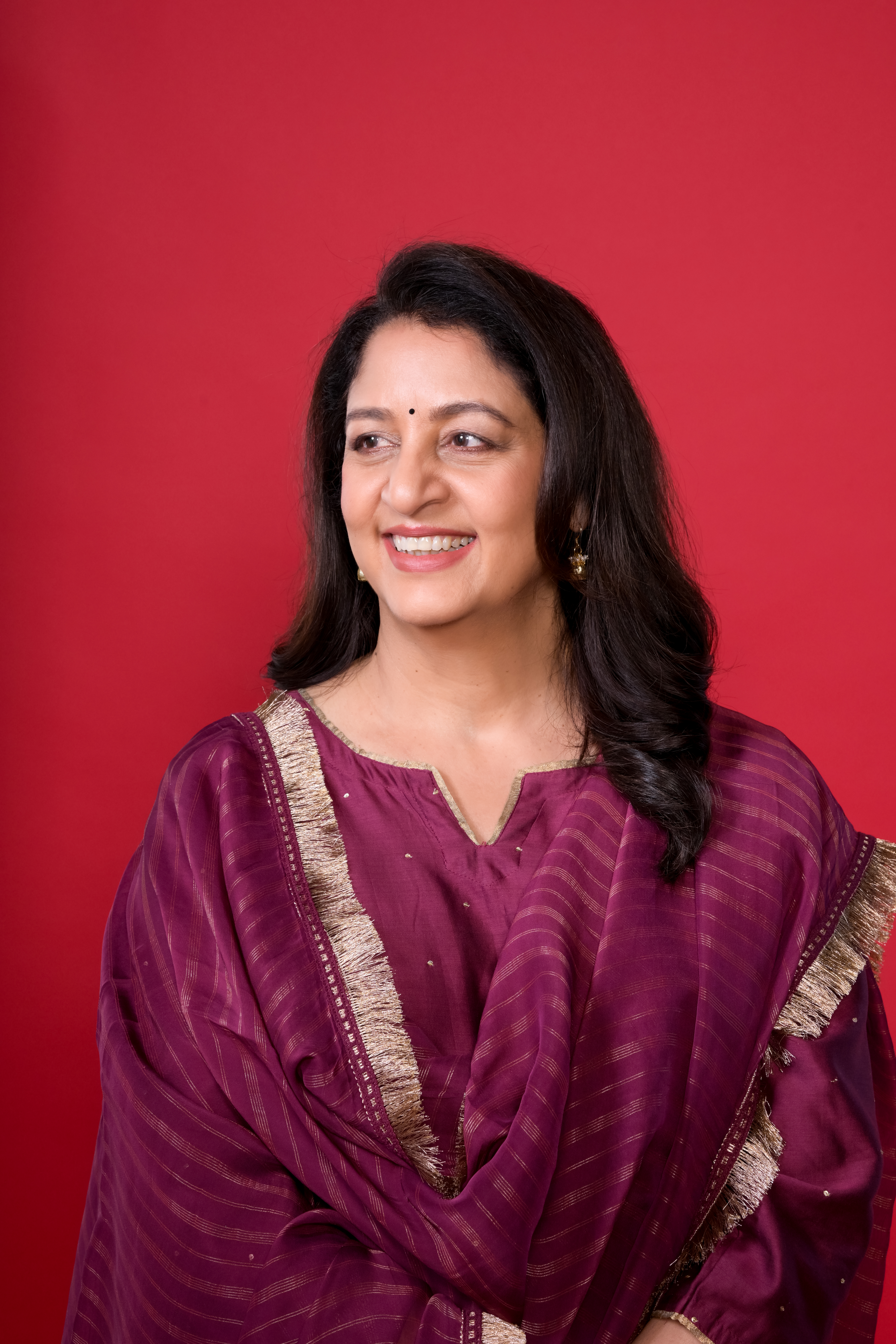 Headshot of Safeena Husain on a red background