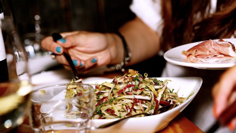 Person eating salad in restaurant uses chopsticks to pick up food