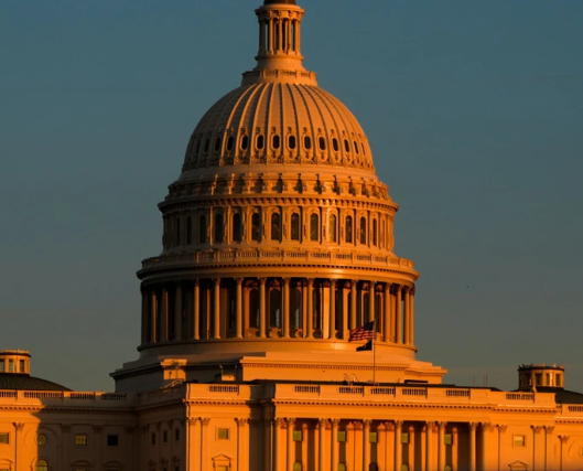 US Capitol building dome in Washington, DC, illuminated by warm sunlight against a clear sky.