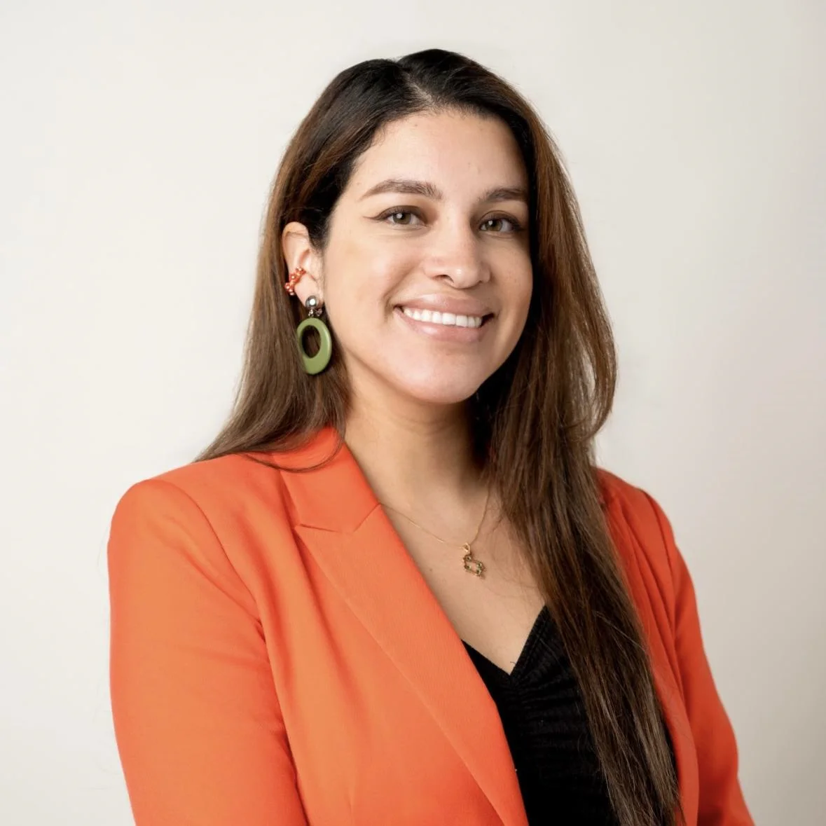 Selena Chávez is facing the camera and smiling. She is wearing an orange jacket.