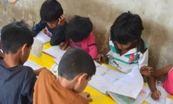 Children studying while siting on a desk with books and notebooks infront of them.