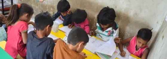 Children studying while siting on a desk with books and notebooks infront of them.