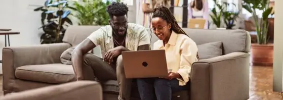 A girl and a guy siting and reading from a laptop.