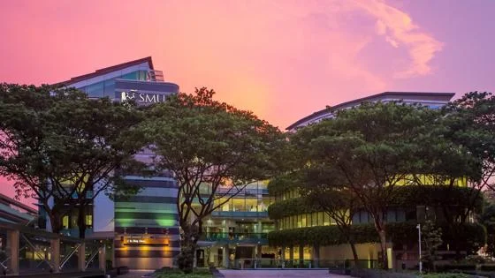 Modern campus buildings at Singapore Management University SMU under a pink and orange sunset sky.