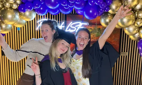 Students at Graduation posing under balloons.