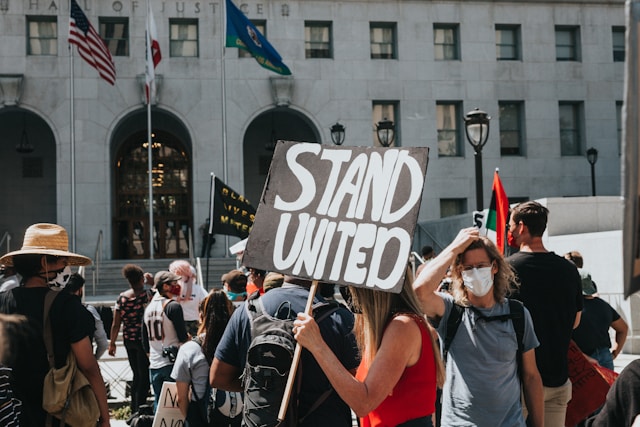 People in standing on street during daytime one is holding a protest sign, which reads "stand united"
