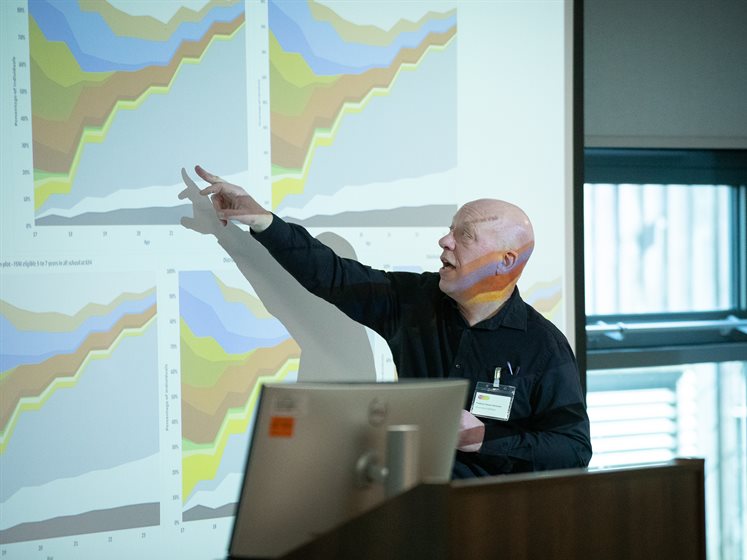 A lecturer pointing to data graphs on a white screen