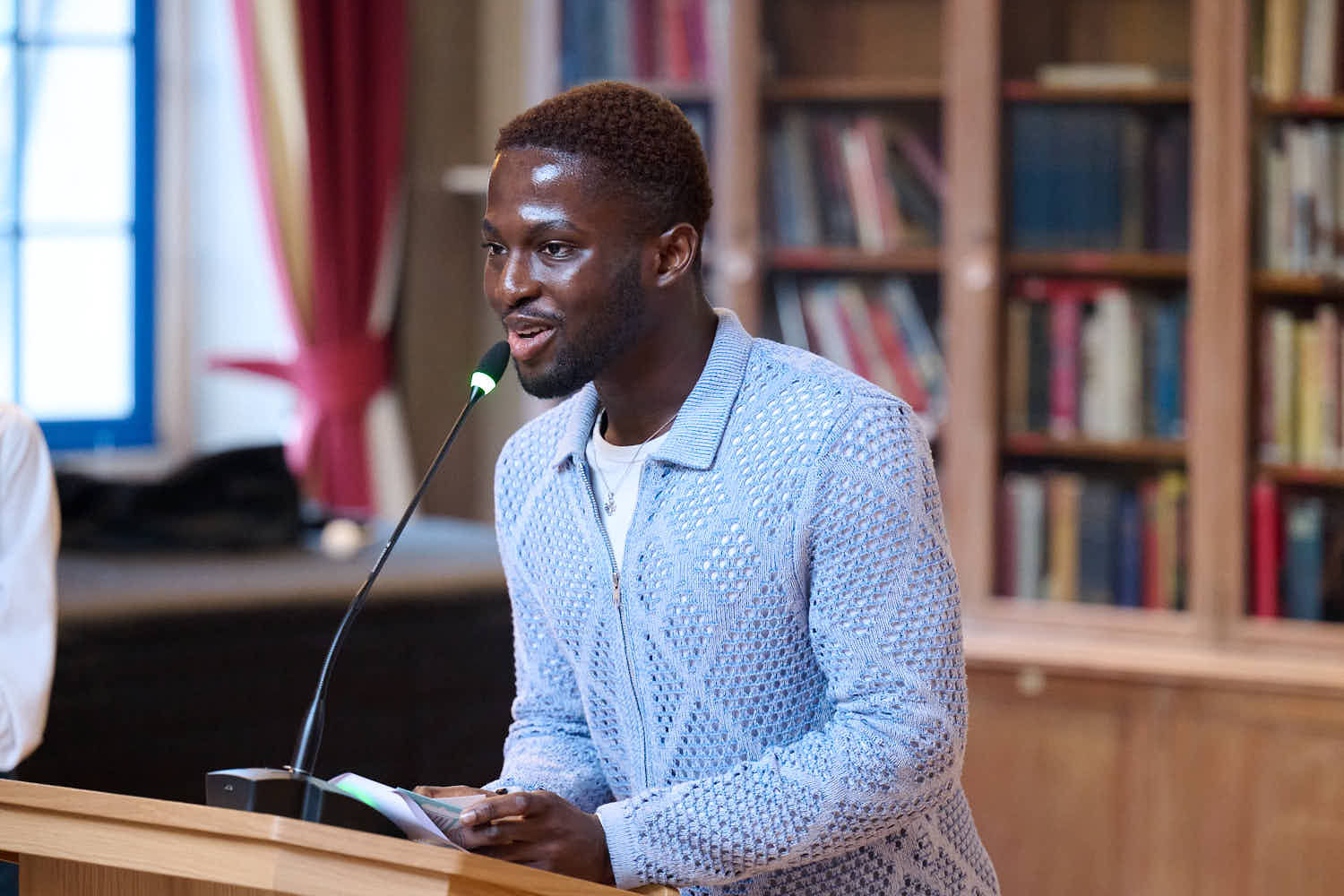 Winner of award, black male student wearing blue cardigan making speech at podium.