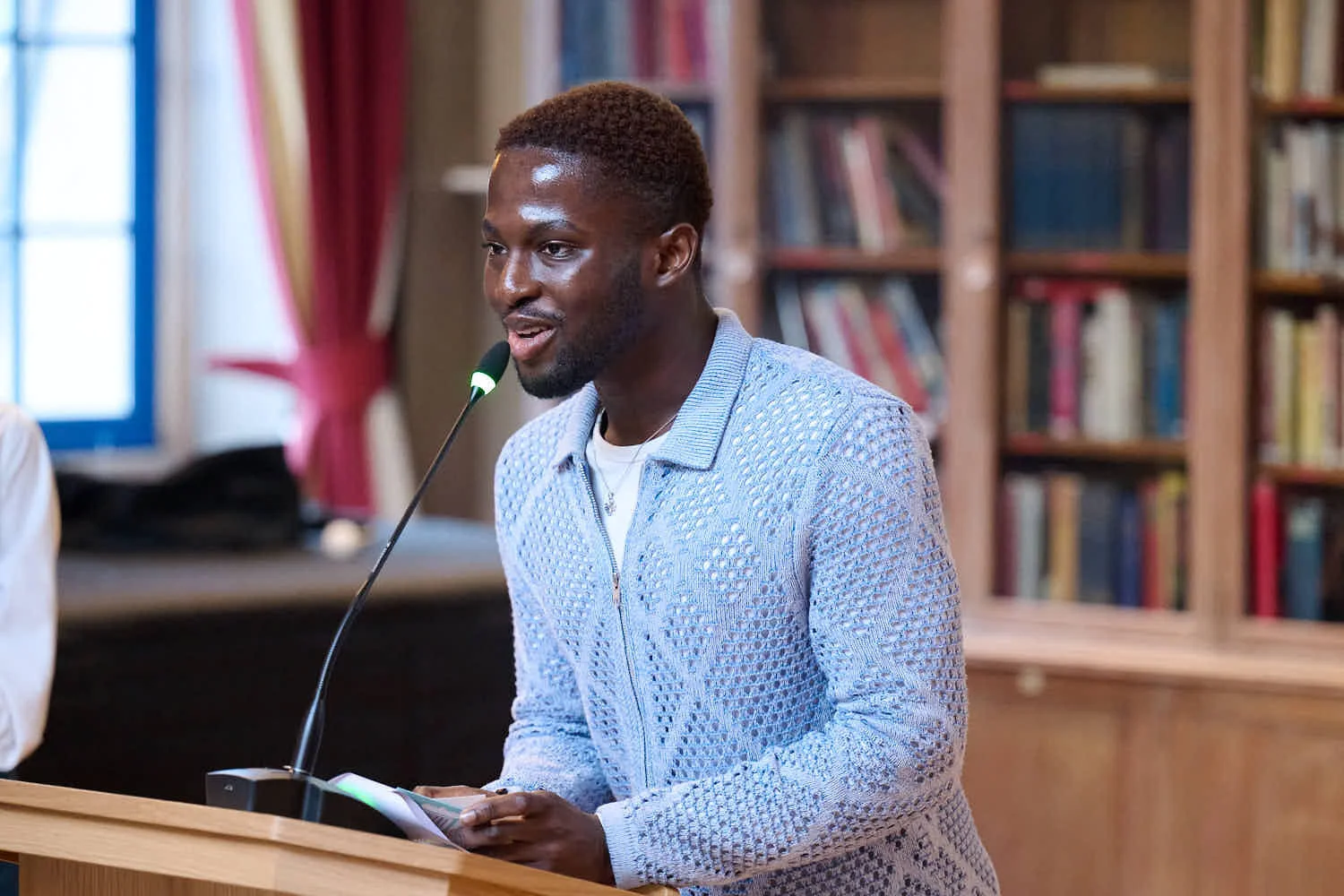 Winner of award, black male student wearing blue cardigan making speech at podium.