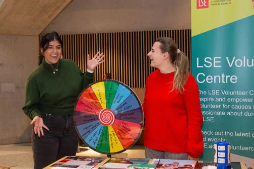 Two students stand with a colourful rainbow spinning wheel
