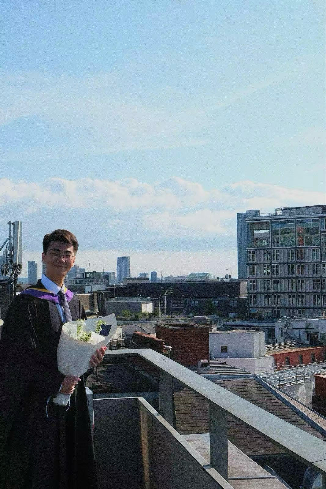 Sung Jae Harry Park is pictured in his LSE graduation gown with a bouquet of flowers and the London skyline in the background.