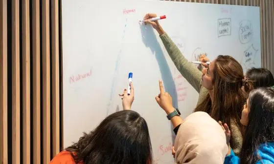 A teacher and class writing on a whiteboard