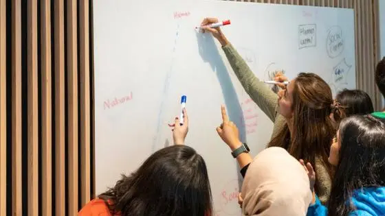 A teacher and class writing on a whiteboard