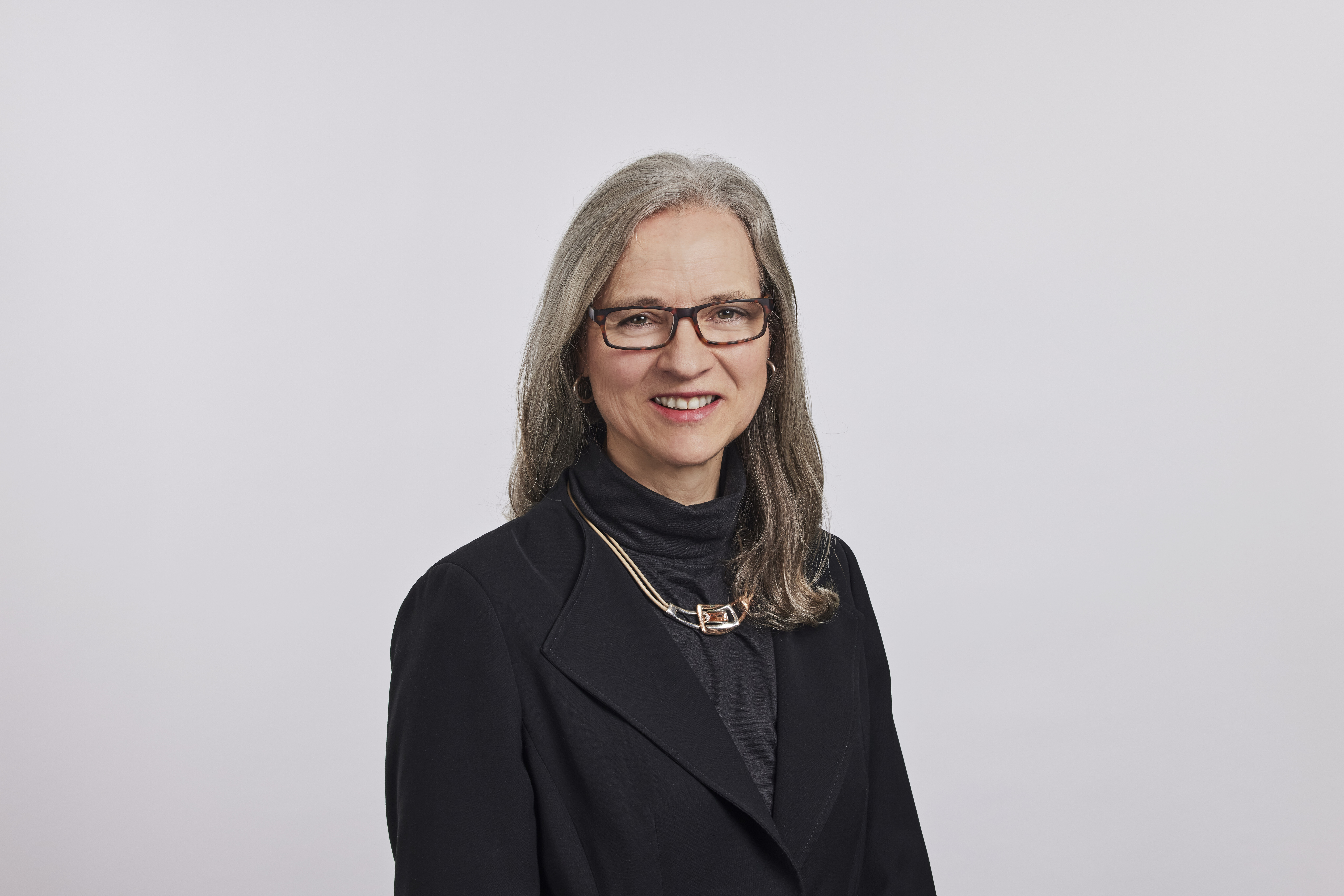 Tess Younger headshot wearing a black blazer and necklace