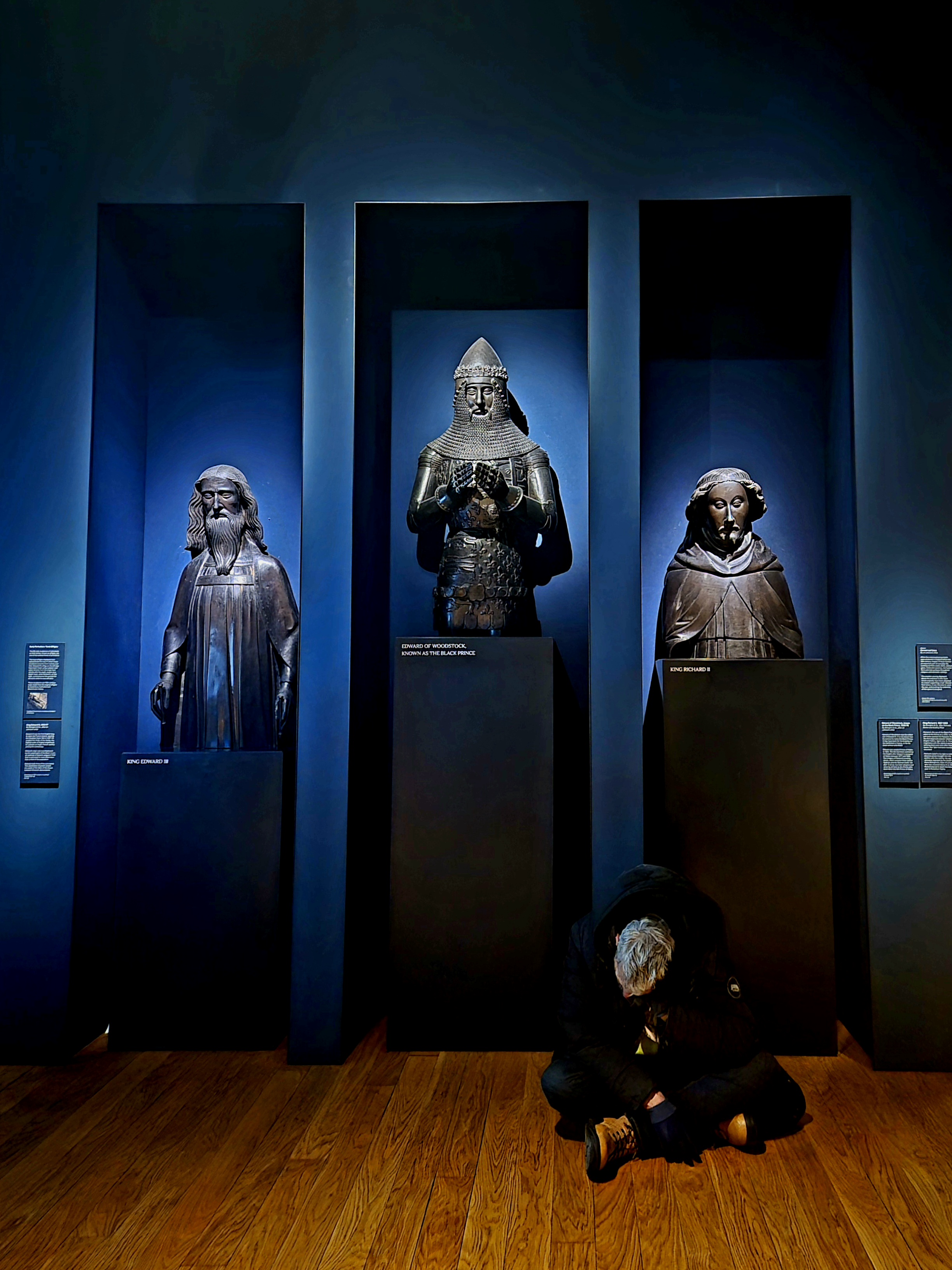slumped sitting person in front of three statues