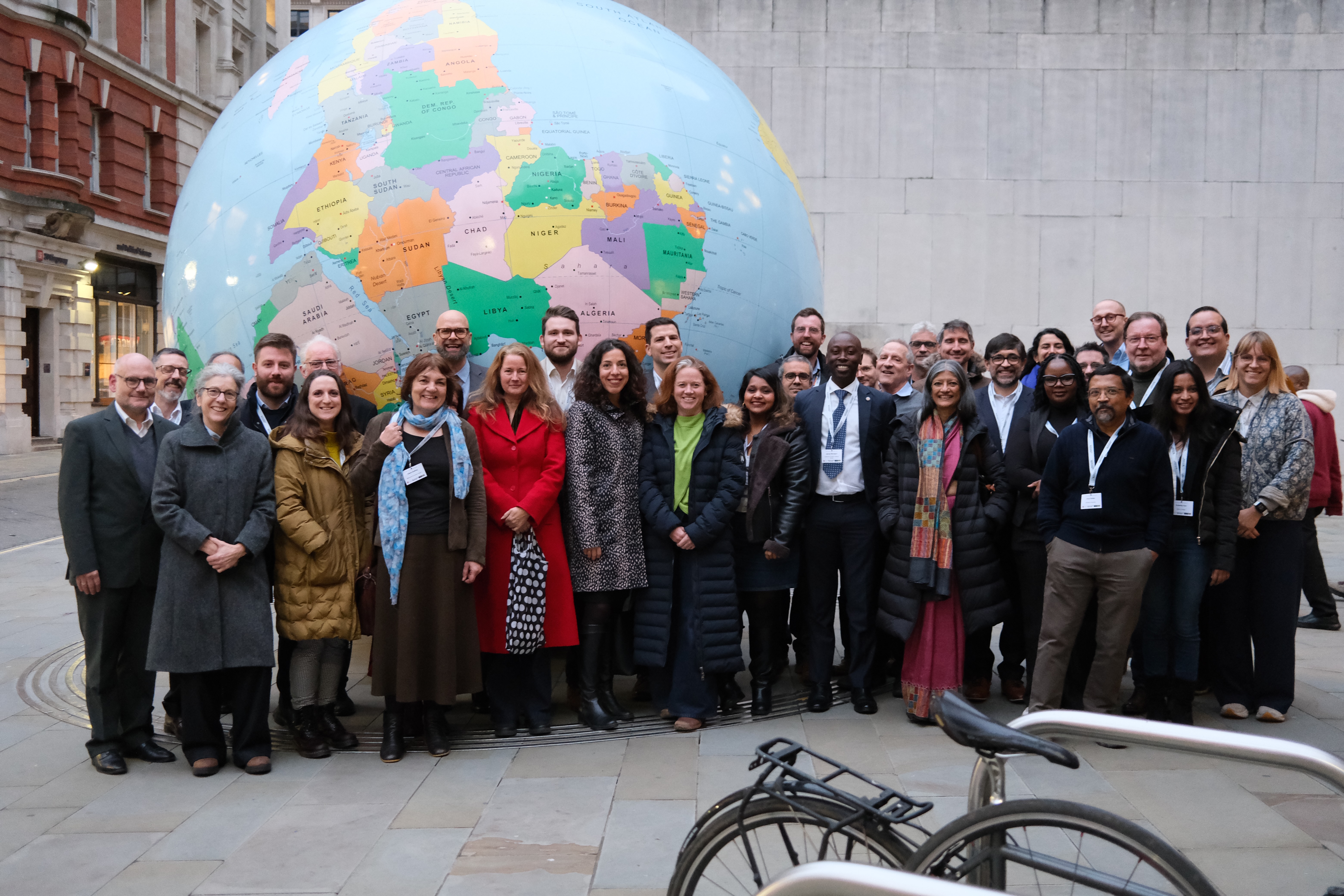 Participants from Too Much Finance conference standing in front of globe sculpture at LSE