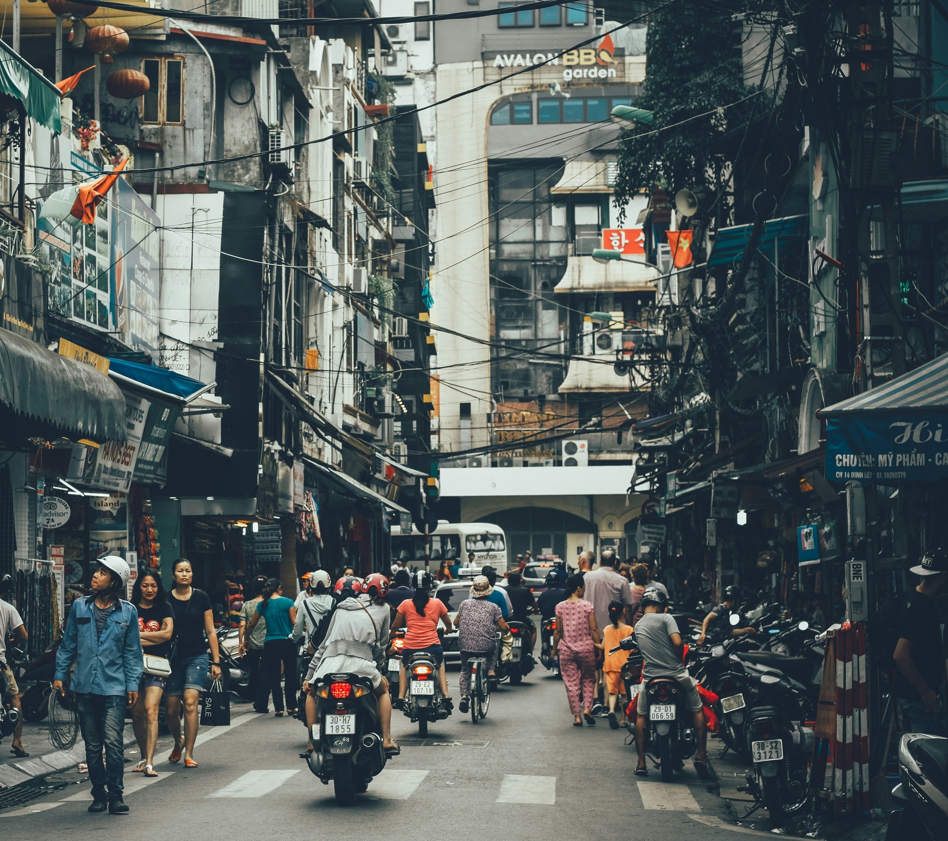 People walking on a rad between buildings, with heavy motorcycle traffic.
