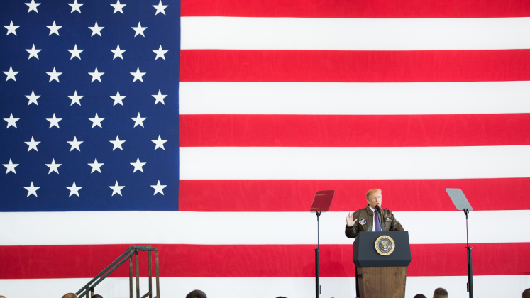 Donald Trump speaking in front of a large US flag