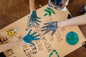 Paint-covered hands coming together over a cardboard sign with drawn symbols highlighting sustainability and recycling