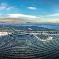 Expansive renewable energy site with rows of solar panels across rolling terrain, alongside multiple tall wind turbines