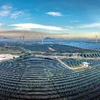 Expansive renewable energy site with rows of solar panels across rolling terrain, alongside multiple tall wind turbines