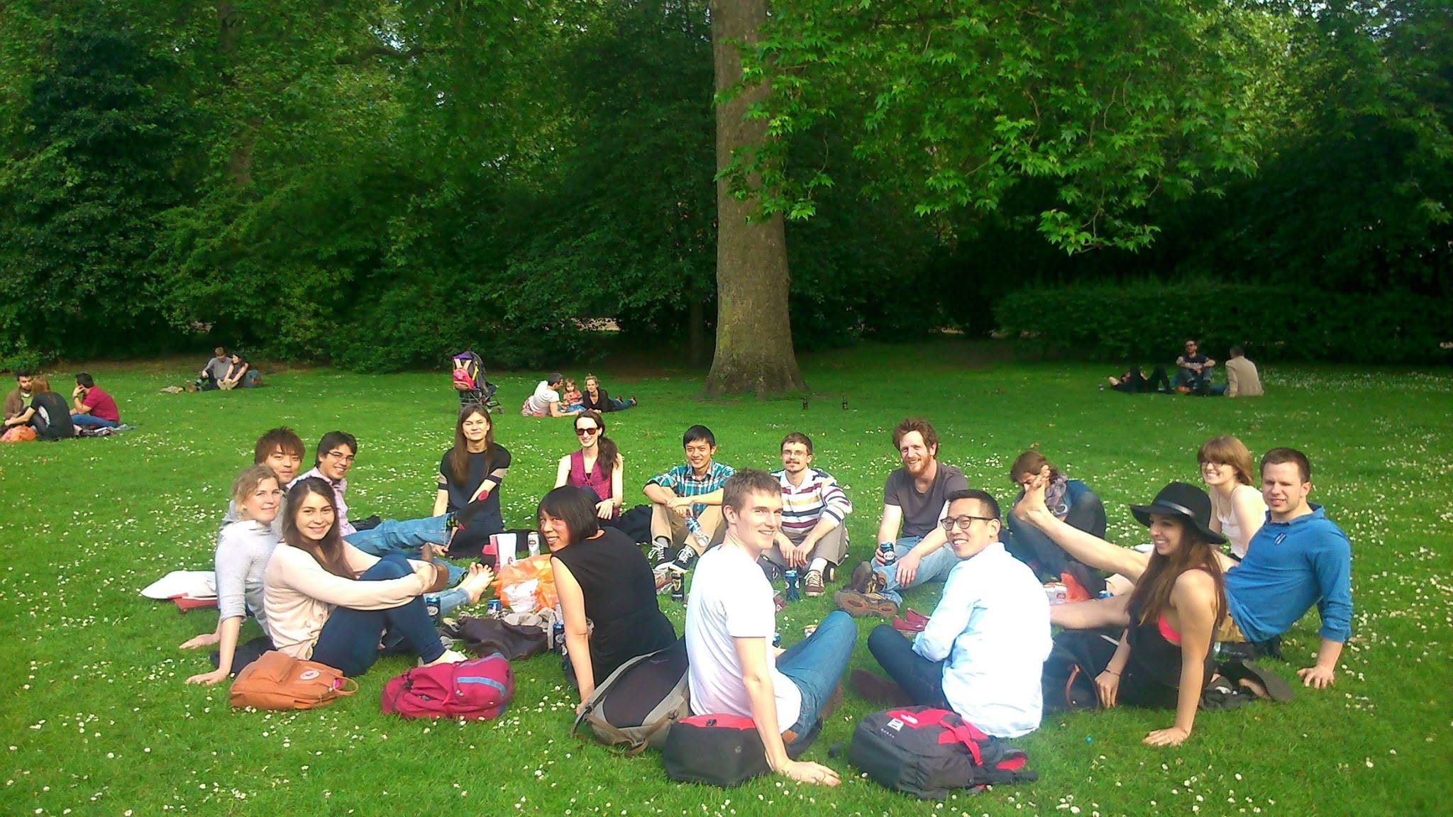 photo of a group of students sat on a grassy lawn, having a picnic