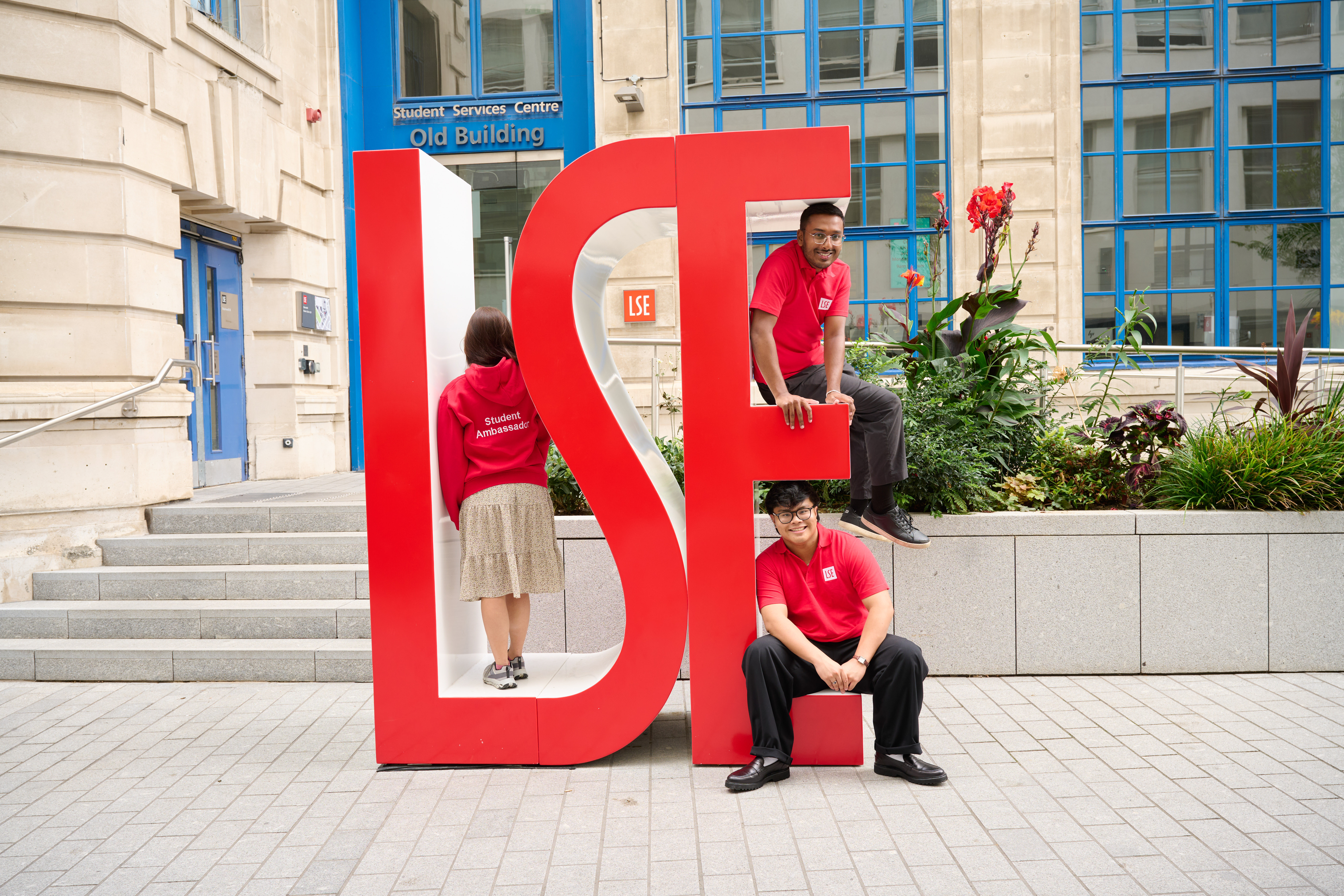 three undergraduate students sit on LSE sign.