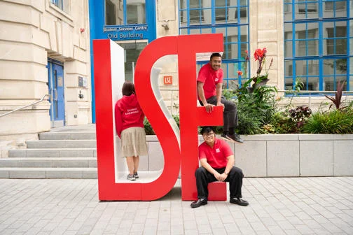 three undergraduate students sit on LSE sign.