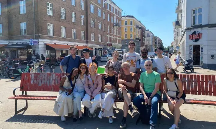 Staff and students sitting on a bench in the city sunshine.