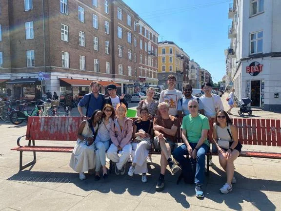 Staff and students sitting on a bench in the city sunshine.