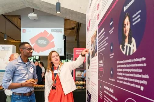 An LSE researcher speaking to a member of the public at the exhibition, pointing at one of the exhibits.