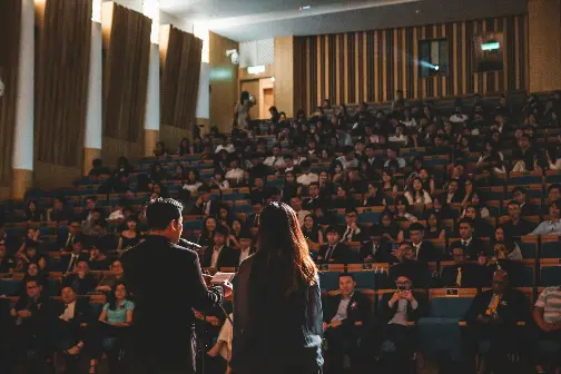 Two speakers giving a lecture to a full audience