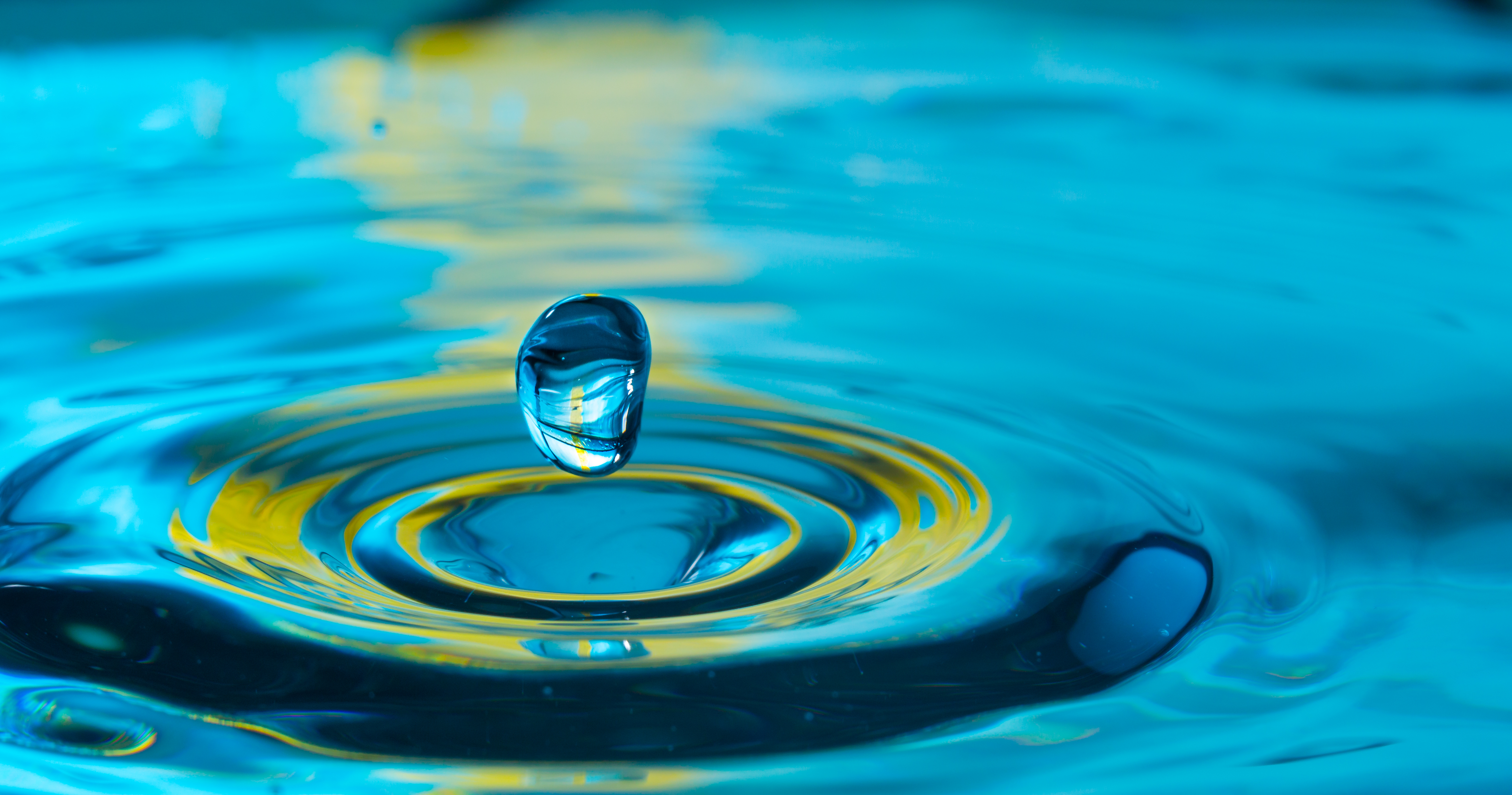 Close-up of water drop splashing into water, green and blue accents.