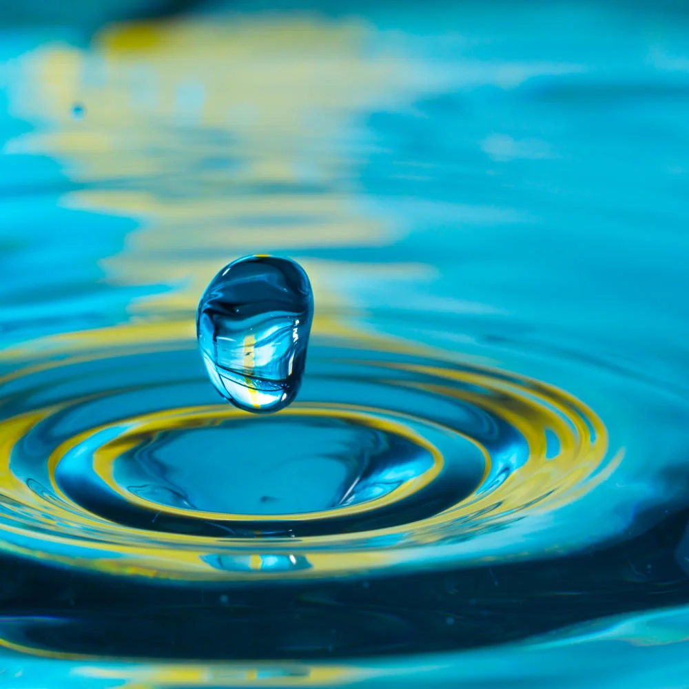 Close-up of water drop splashing into water, green and blue accents.