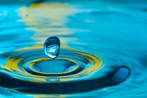 Close-up of water drop splashing into water, green and blue accents.