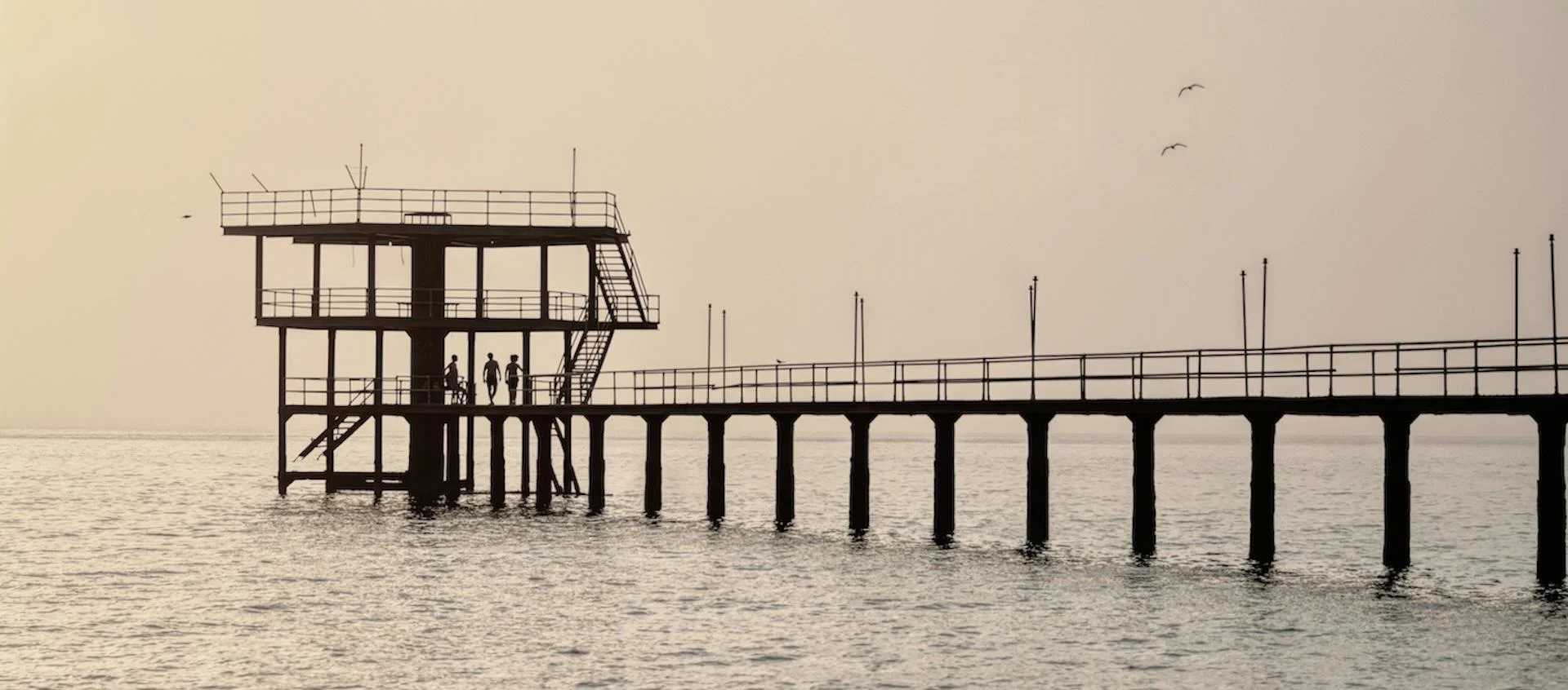 Silhouette of a dock with three figures stood on it.