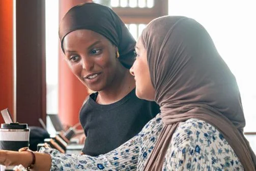 Two female students looking at laptops and chatting
