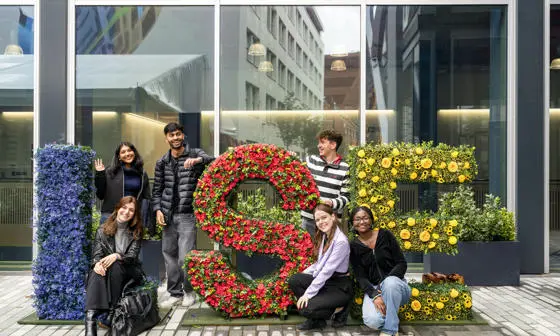 Students standing next to LSE letters decorated with flowers in blue, red and yellow.