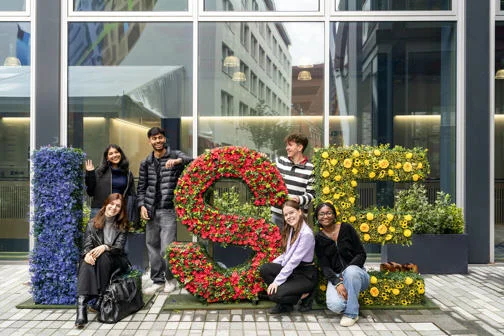Students standing next to LSE letters decorated with flowers in blue, red and yellow.