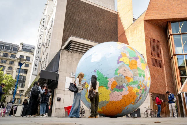 Students standing in front of "The World Turned Upside Down" sculpture by Mark Wallinger, on the LSE campus