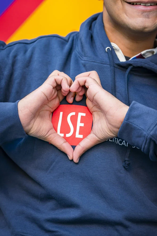 Student forming a heart symbol with their hands around the LSE logo